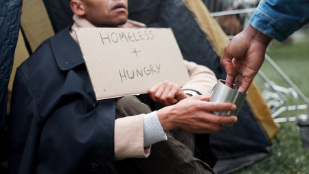 Homeless, person and hands with sign for money with financial donation, compassion and assistance. Beggar, hungry and board by tent with vulnerability, struggle and help with cash for poverty supportの写真素材
