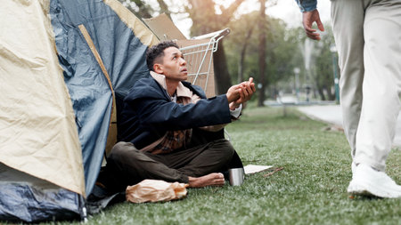 Homeless man, poverty and begging at park by tent for help, donation or kindness from society. Person, hope and ask for money, change or coins for financial crisis, jobless or bankruptcy on groundの写真素材