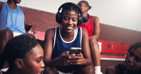Phone, smile and headphones with black woman on basketball court for sports progress, athlete scouting and streaming. Score tracking, training program and subscription with person and game updatesの写真素材