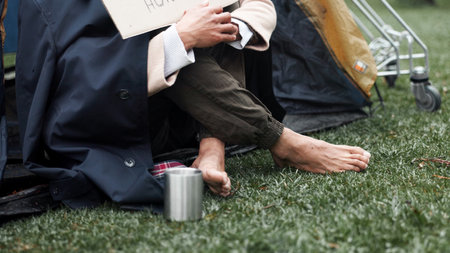 Homeless, poverty and cold with feet of person in park for depression, unemployment rate and crisis. Mental health, refugee and welfare aid with closeup of beggar and tent for tired, poor and worryの写真素材