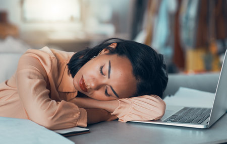 Tired woman suffering from burnout at work, sleeping at desk and napping after meeting a deadline in an office alone. Business woman and corporate professional resting, taking a break with laptopの写真素材