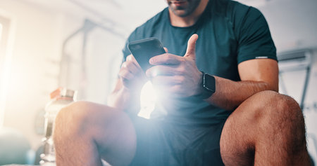 Fitness, hands and man with phone on break to chat on social media, health app or gym blog. Bodybuilding tips, research or athlete with mobile technology reading workout plan for training or exerciseの写真素材