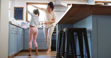 Happy, mother and child dancing in kitchen with holding hands, spinning or teaching steps. Family, woman dancer or girl kid with music for movement, learning and relationship with love, care or trustの写真素材