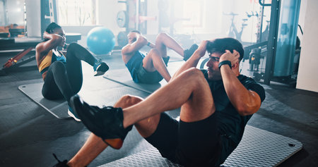 Workout, people and sit ups with personal trainer, class and gym for training or fitness routine. Coaching, goals and target with group of sports exercise in health club together for core muscleの写真素材