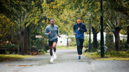 Workout, rain and men running in road for marathon training, endurance challenge and discipline with cardio exercise. People, teamwork and runner club with race, morning jog and wellness in natureの写真素材
