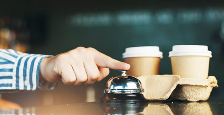 Person, hands and bell with coffee for service, customer attention or signal on cafe counter....