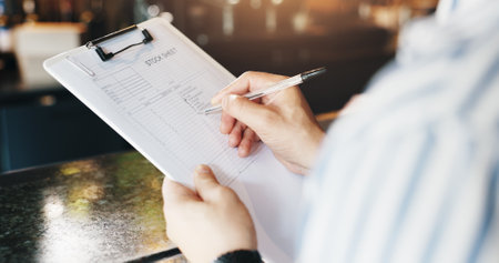 Person, hands and writing with inventory at cafe for stock sheet, checklist or catering service. Closeup, small business owner or manager with inspection or notes for order or products at coffee shopの写真素材