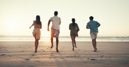 Running, sunset and back of people on beach for tropical vacation, break or holiday together. Freedom, energy and group of friends by ocean for seaside weekend trip for travel with activity in summerの写真素材