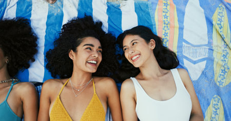 Friends, happy women and relax on blanket at beach for vacation, holiday and travel with top view. Girls, smile and outdoor together at coast above for funny conversation, laugh or bonding in summerの写真素材