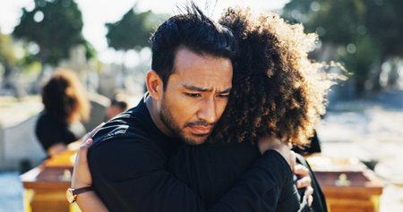 Hug, sad and funeral with people, graveyard and grief with emotion, mental health or sorrow. Ceremony, outdoor or family with loss, support or comfort with compassion, mourning or empathy with burialの写真素材