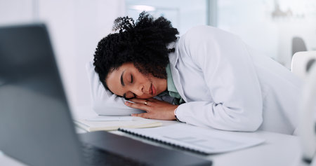 Tired woman, scientist and sleeping with laptop at laboratory for fatigue, burnout or overworked. Female person, asleep or rest with science documents on computer for nap, dream or exhausted on deskの写真素材