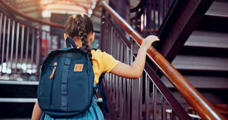 Walking, stairs and child in library for education, story literature and learning at school. Academy, young student and girl with backpack for knowledge, back and language development for growthの写真素材