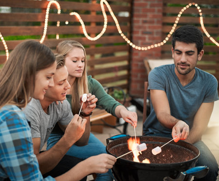 Fire, fun and people roasting marshmallows in backyard for social event, gathering or hang out. Grill, flame and group of friends toasting, burning or melting sweet treat for smores snack outdoor.の写真素材