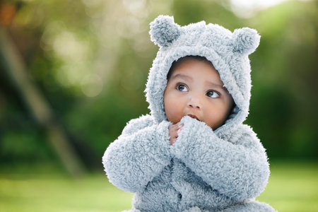 Baby boy, adorable and cute with jacket in nature for fashion, cotton or furry outfit. Little infant, innocent child or kid thinking in wonder or thought with bear ears for outdoor childhood at parkの写真素材