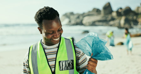 Happy man, volunteer and cleaning beach with bag for recycling, eco friendly environment or earth day. Male person, activist or community service with smile or dirt for save planet or world charityの写真素材