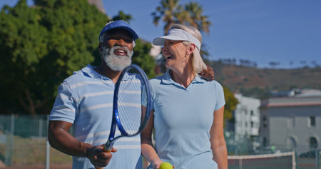 Tennis court, interracial couple and mature people laugh for fitness, game joke or competition. Training, racket and funny man with woman for match, workout and weekend hobby for health and wellnessの写真素材