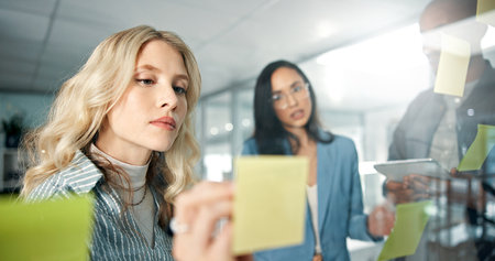 Business woman, writing and sticky note with team, brand strategist for brainstorming and market research on tablet. People in collaboration, solution and social media project plan with idea on glassの写真素材