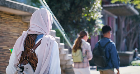 University, students and woman in hijab walking from back with diversity, backpack and study in education. Culture, equality and Muslim college girl on campus for morning commute to school with groupの写真素材