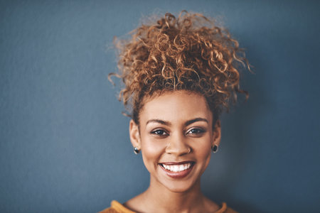 Portrait, happy and woman with piercings in studio for alternative style, fashion and confidence. Positive, smile and face of female person with cosmetic, makeup and jewellery on blue backgroundの写真素材