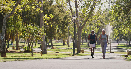 Fitness, elderly couple and running in park for training, cardio exercise and wellness in retirement. Senior interracial people, smile outdoor or workout support, motivation or friends with energyの写真素材