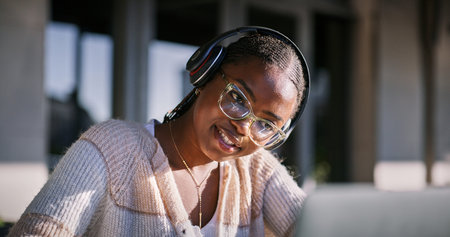Glasses, headphones and black woman with laptop, smile and listening to audio, video editing and...