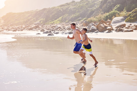 Father, son and running at beach for vacation, bonding or love in summer, outdoor and together in nature. Dad, child and playful with care, holiday or people with family in sunshine by ocean in Spainの写真素材