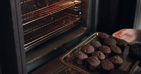 Muffins, cooking and hands with tray from oven, kitchen or morning in bakery with process or production. Baking, dessert or person with cupcakes for a delicious snack, pastry or prepare food in homeの写真素材