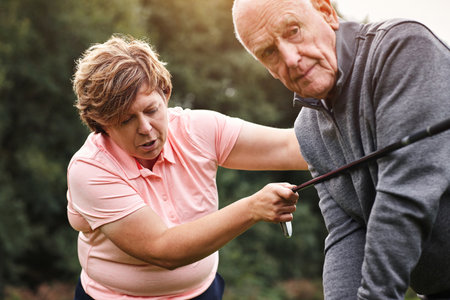 Golf course, coach and senior man learning at club, field or outdoor in nature to help at lesson. Golfers, instructor and teaching elderly person, exercise or training together for sports in summerの写真素材
