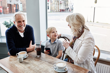 Happy and family, grandparents with kid at cafe for conversation, talking of holiday visit in London. Senior people with boy or child at coffee shop for discussion, funny chat and planning at tableの写真素材