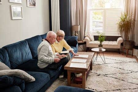 Senior couple, documents and planning budget on sofa for investment, assets and bills at home. Man, woman and check paperwork for insurance information, mortgage loan and reading retirement savingsの写真素材