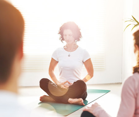 Yoga instructor training people during a fitness class in a studio. Female yogi teaching breathing techniques with mindful meditation exercises for zen energy in lotus pose during a lesson indoorsの写真素材