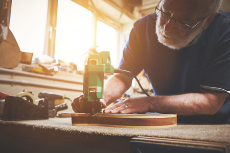 Skilled, creative and professional carpenter making wooden guitar in a workshop. Expert entrepreneur...