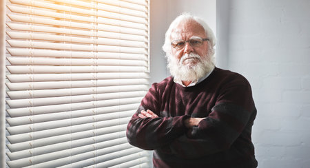 Senior man standing with arms crossed, looking angry and unhappy at home. Portrait of the face of a mature, retired and expert professor with arms folded, frowning and looking serious in an officeの写真素材
