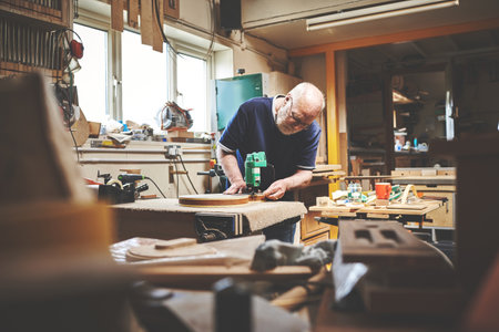 A senior handyman working in his home garage or workshop cutting or sanding wood. Skilled mature male craftsman building, repairing or cutting a piece of wood in his woodwork shopの写真素材