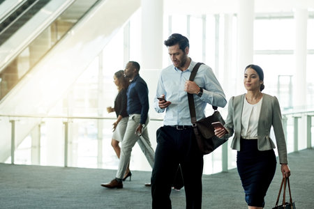Business, people and walking with phone at airport for flight schedule, booking information and airplane arrival. Professional, team and travel in lobby for corporate journey and global conferenceの写真素材