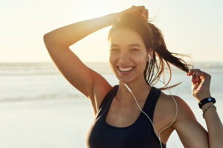 Fitness portrait, beach and smile with woman prepare for running, workout and summer with music. Athlete, ponytail and ready to start jog for exercise, endurance or health for wellness sport trainingの写真素材