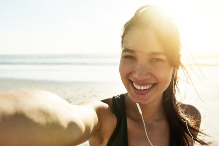 Woman, selfie and happy for exercise at beach, portrait and excited for post on web with fitness at sunrise. Girl, person and smile with earphones, streaming and listen to music for workout in Italyの写真素材