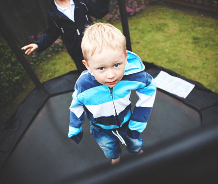 Above view of a young male child playing on a trampoline outside. A small boy being active jumping outdoors in their family garden. Cute little kid spending time in the green outdoorの写真素材