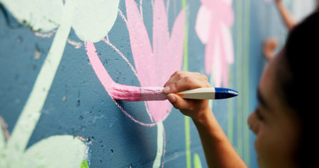 Woman, hand or painting on wall art for mural, creativity or community service at building. Artist, paintbrush or outdoor with color for floral decor, creative process or flowers for aesthetic designの写真素材