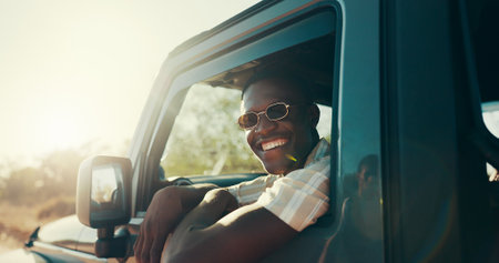 Black man, road trip and happy with sunglasses by window with driving, journey and excited for safari in summer. African person, smile and face in vehicle, transport and travel at sunset in Kenyaの写真素材