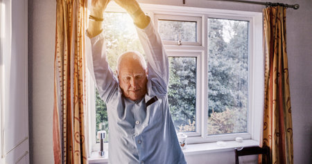 Senior man stretching arms in home bedroom, relax or body health in the morning. Elderly person wake up for wellness, comfort and awake to start fresh day in pajamas in retirement, apartment or houseの写真素材
