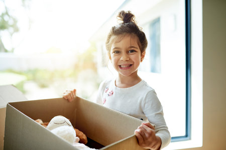 Box, portrait and smile of girl in new home on moving day, excited for child development or growth. Happy, property and real estate with cute kid carrying package in apartment for relocationの写真素材