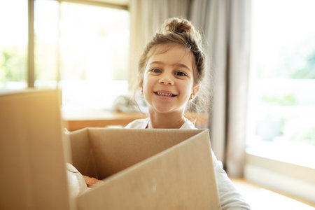 Portrait, real estate and happy kid with box in new house, unboxing or pack for relocation to dream property. Face, moving or girl child with cardboard for donation, storage or carry toys for charityの写真素材