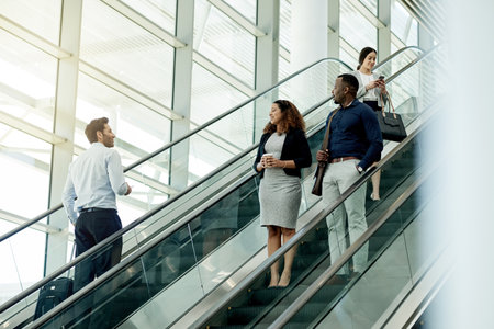 Business, people or travel on escalator in lobby for morning commute, conference arrival or international expo. Professional, group or greeting on moving staircase for corporate journey or colleaguesの写真素材