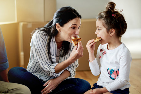 Moving, mother and child eating pizza in new home to celebrate real estate loan or mortgage on floor. Family, parents and kid with fast food for relocation, unpacking break or share meal in propertyの写真素材