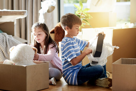 Home, children and packing toys in cardboard, boxes and helping relocation on living room floor. Siblings, real estate investment and together in new house, dream property and moving out apartmentの写真素材