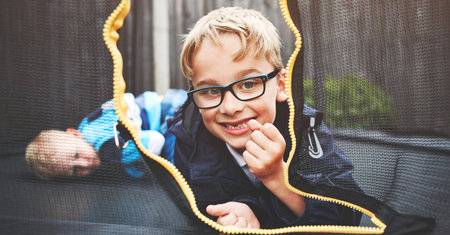 Happy and smiling child lying on a trampoline with a friend, brother or family member portrait. Cute little children relaxing after playing outside, having fun and being active on play dateの写真素材