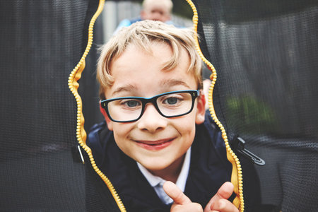 Cheerful, happy and playful little boy jumping on a trampoline outside. Portrait of a smiling child looking through the safety net entrance. Charming kid enjoying play time in nature with a friend.の写真素材