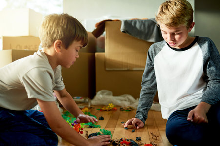 Boxes, moving and children with toys in new home for fun, bonding and sibling time for development. Growth, cardboard and boy kid teaching brother to play with trinkets for game in family house.の写真素材