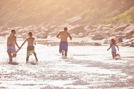 Water, kids and parents running on beach for fun, travel holiday or bonding together on tropical adventure. Waves, energy and family playing on island vacation with ocean, splash and summer from backの写真素材